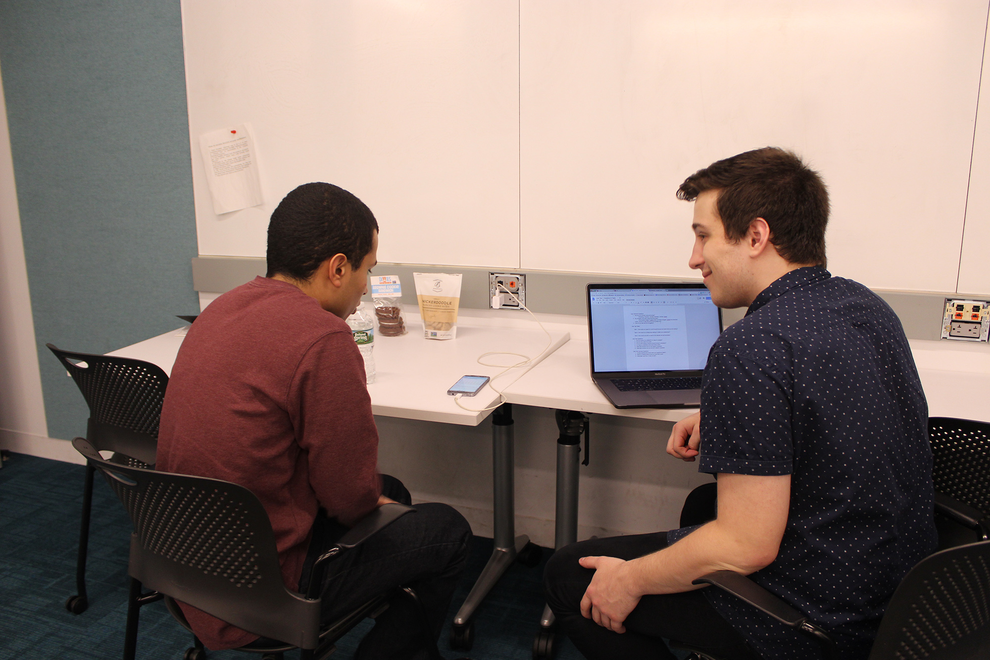 two men sitting next to each other with laptop inbetween
